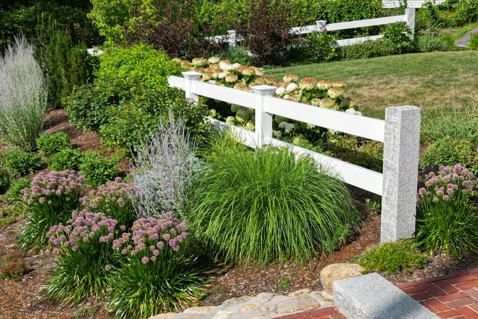 Ornamental grasses along this garden fence in Carlisle add privacy, movement, and a natural buffer while blending seamlessly with edible plantings.