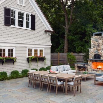 Outdoor dining space combining a stone fireplace and grill, extending usability into cooler evenings with warmth and visual focus.
