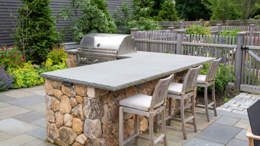 Custom stone patio designed for outdoor cooking, featuring a grill positioned near dining areas for easy serving and casual backyard meals.