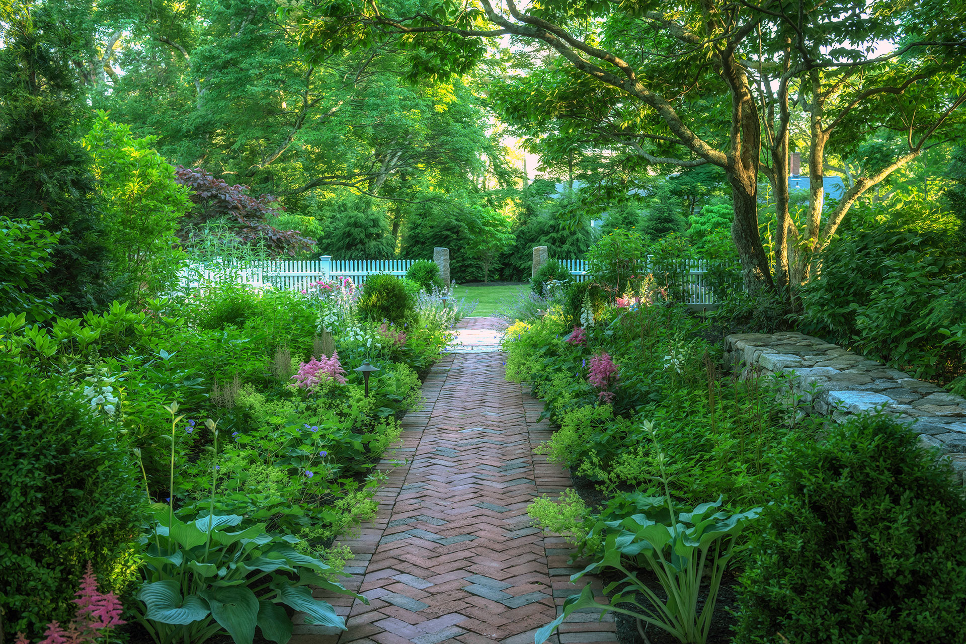 Brick herringbone path adds texture and tradition, guiding movement through shaded planting in Weston.