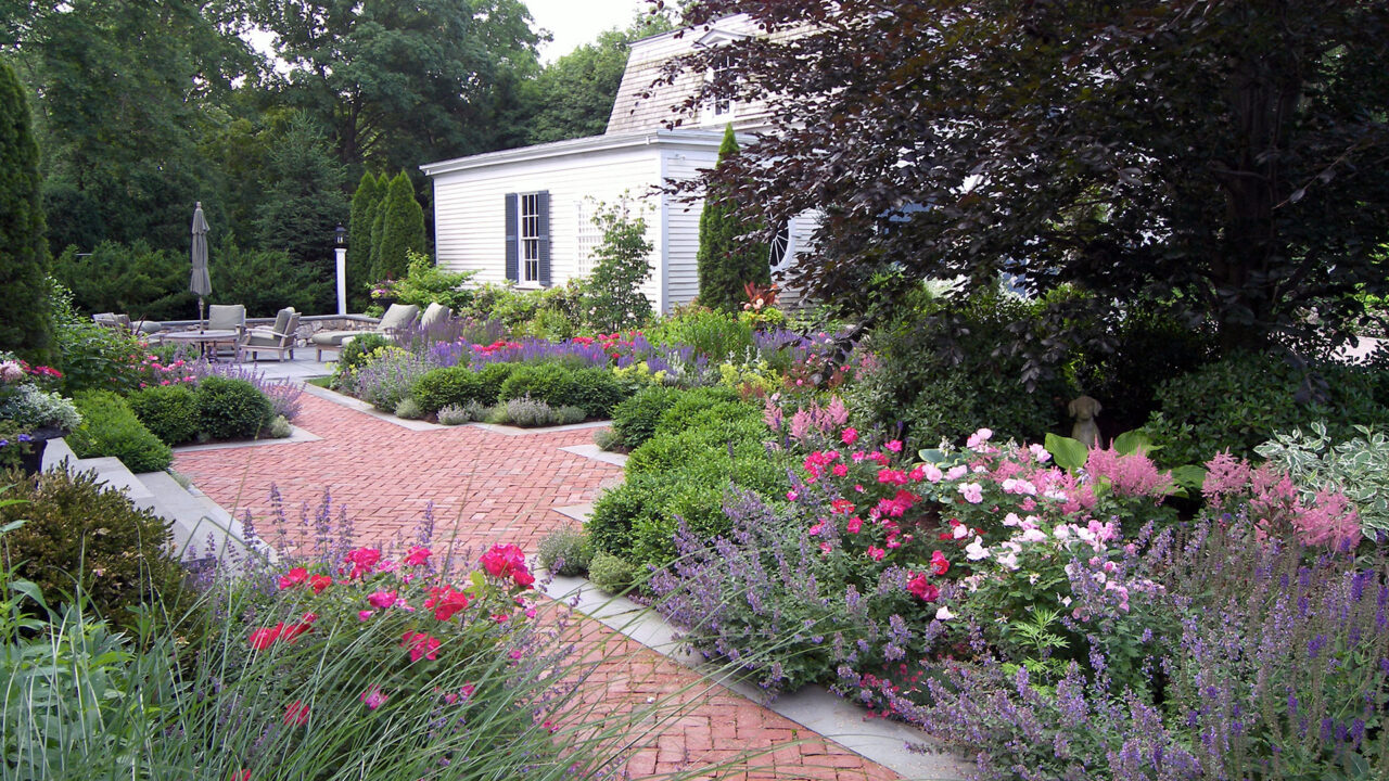 A brick garden path flows through lush perennials, blending structure with classic estate-style planting.