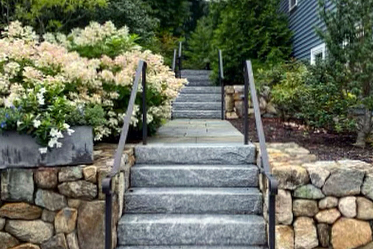 Granite front steps with iron railings and fieldstone walls provide safe, timeless access with strong curb appeal.