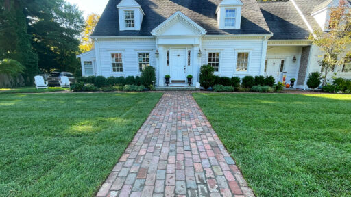 Straight reclaimed brick walkway delivers timeless curb appeal, guiding guests cleanly to the front door with warmth and New England character.