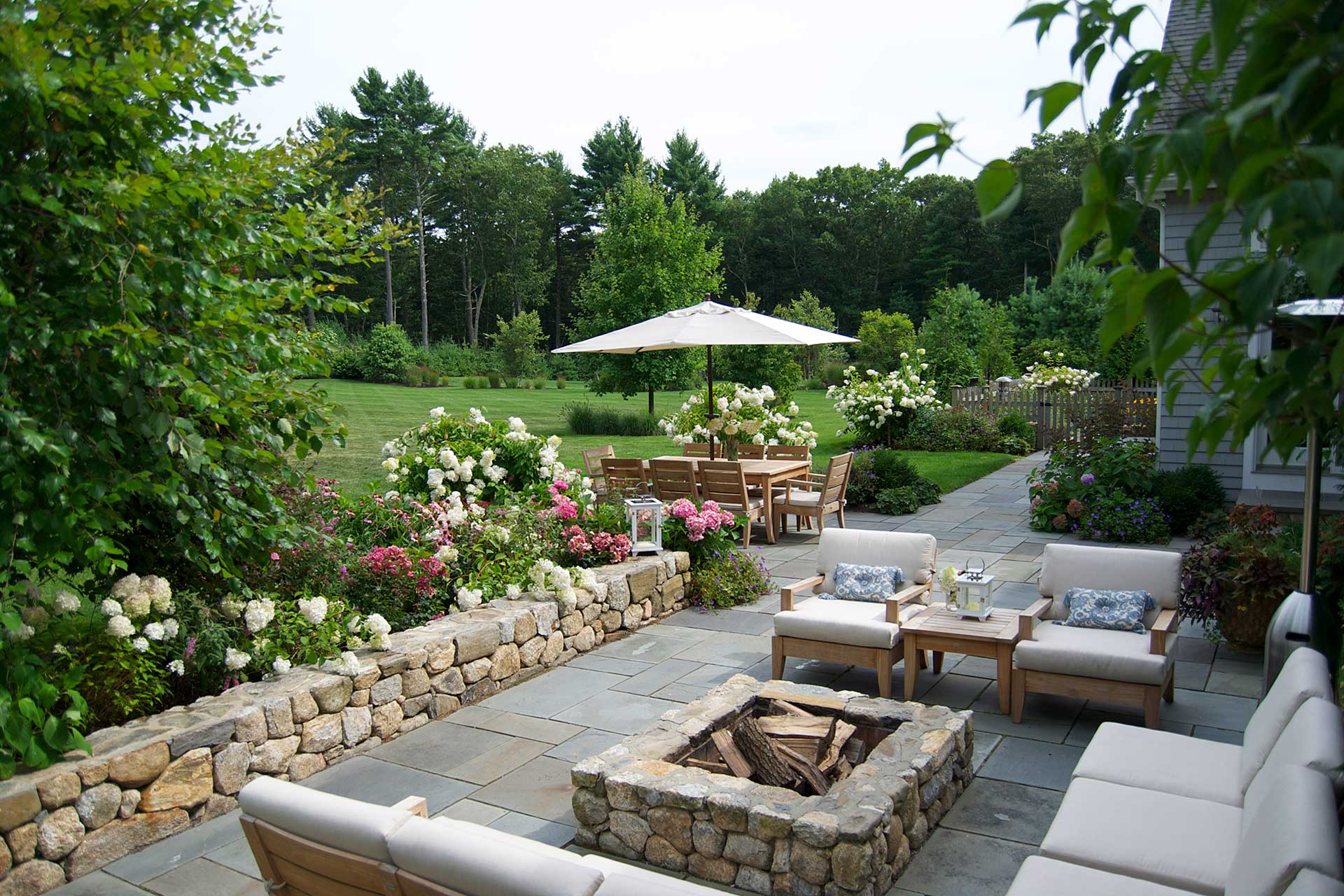 Bluestone firepit terrace with garden beds and outdoor dining melds functional entertaining space with layered planting and stone craftsmanship.