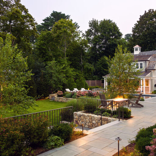 Elevated bluestone terrace accented with evening lighting and a fire feature sets a warm, inviting mood for entertaining after dusk in Weston gardens.