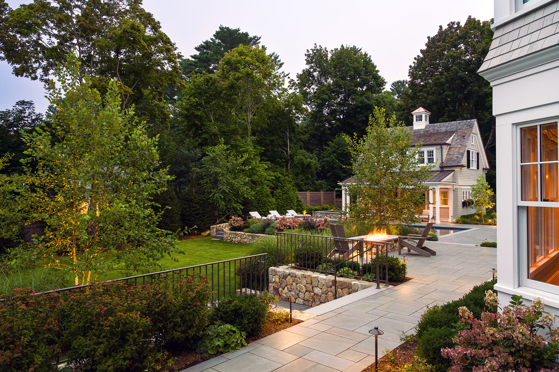 Elevated bluestone terrace accented with evening lighting and a fire feature sets a warm, inviting mood for entertaining after dusk in Weston gardens.
