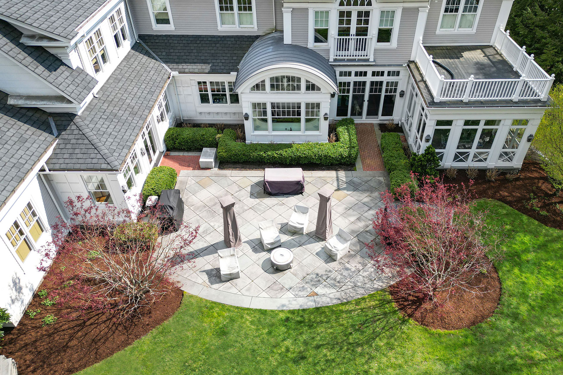 Large oval bluestone patio with distinct lounge zones and spring colors brings expansive outdoor living space to life with seasonal blooms.