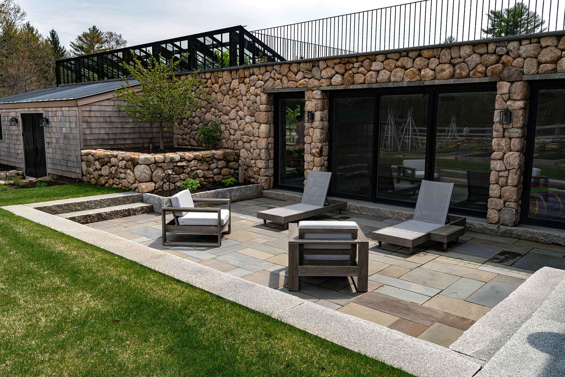 Modern stone terrace with lounge chairs and retaining walls offers a minimalist yet refined outdoor setting with clean lines and calm garden views.