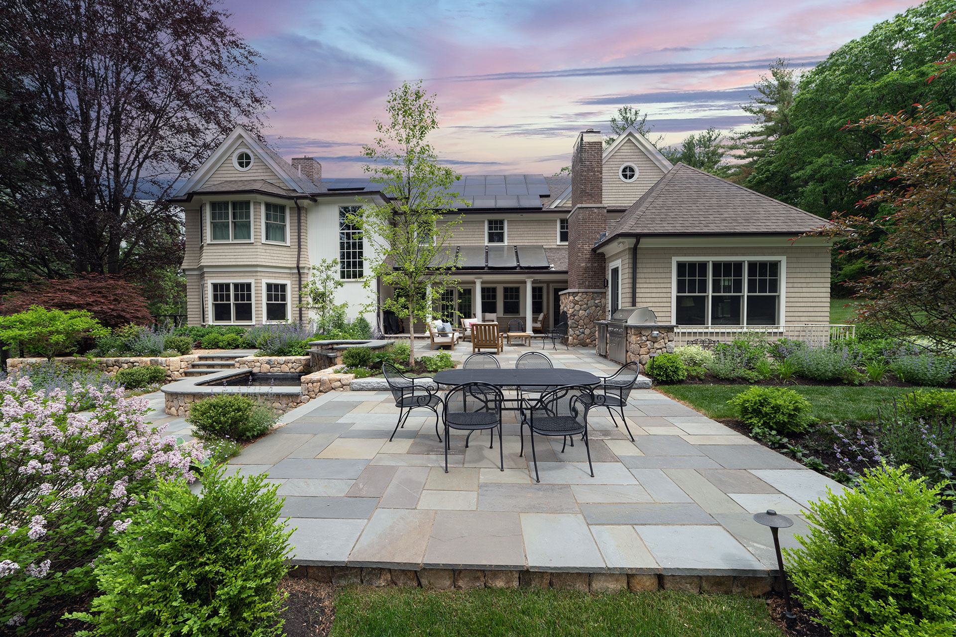 Multi‑tiered patio with water feature and sunset sky frames elegant outdoor seating, blending stonework with tranquil design elements.