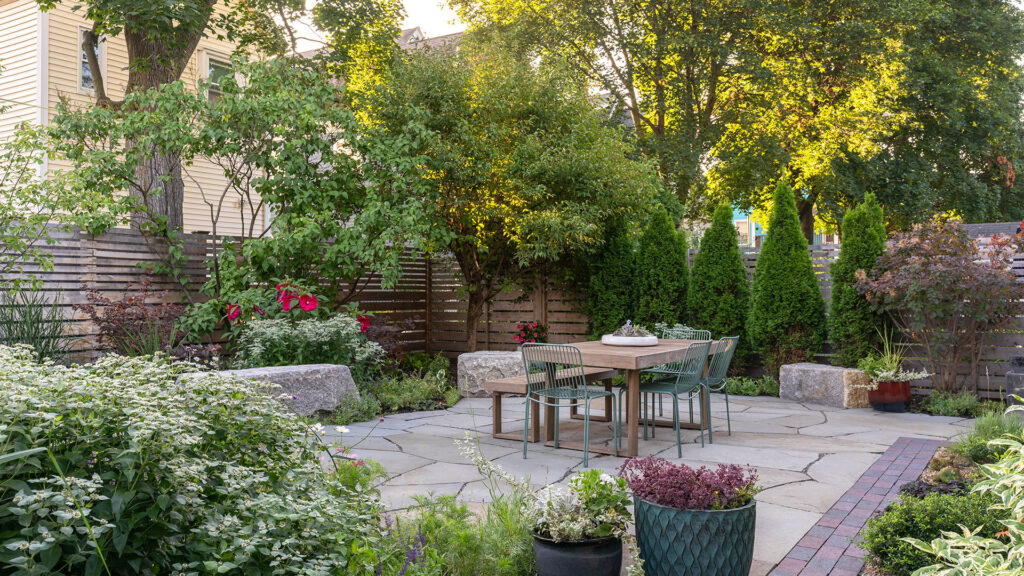 Small garden patio with lush perennial borders and privacy trees creates a serene urban escape with natural stone paving and cozy seating.