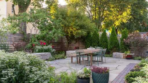 Small garden patio with lush perennial borders and privacy trees creates a serene urban escape with natural stone paving and cozy seating.