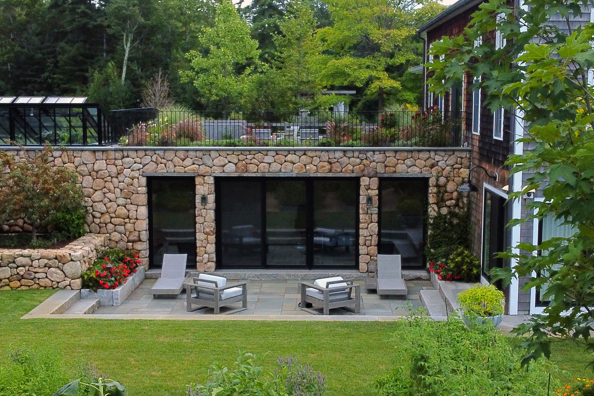 Small seating terrace framed by fieldstone walls overlooks a manicured lawn, offering an intimate outdoor retreat with classical stone charm.