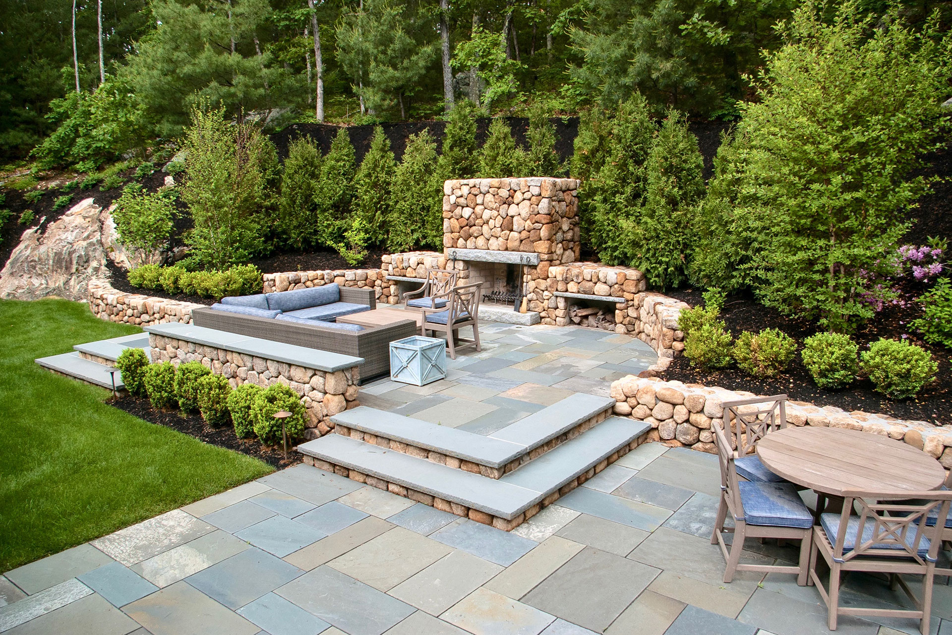Tiered stone terrace with integrated outdoor fireplace and steps offers warmth and ambiance, perfect for cool evenings and social gatherings around firelight.