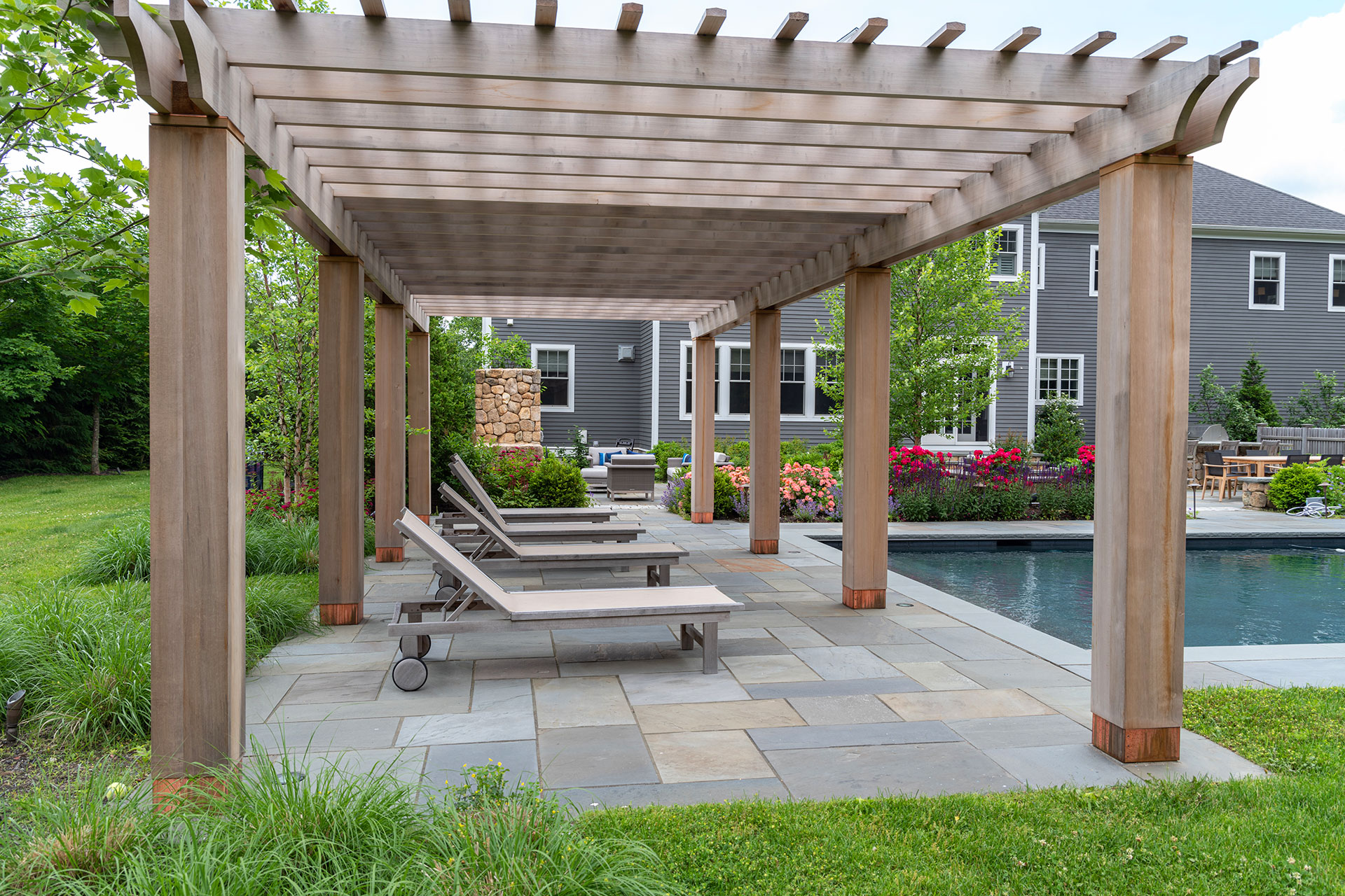 Cedar pergola provides natural shade near the pool, softening hardscape edges while aging gracefully in a New England climate.