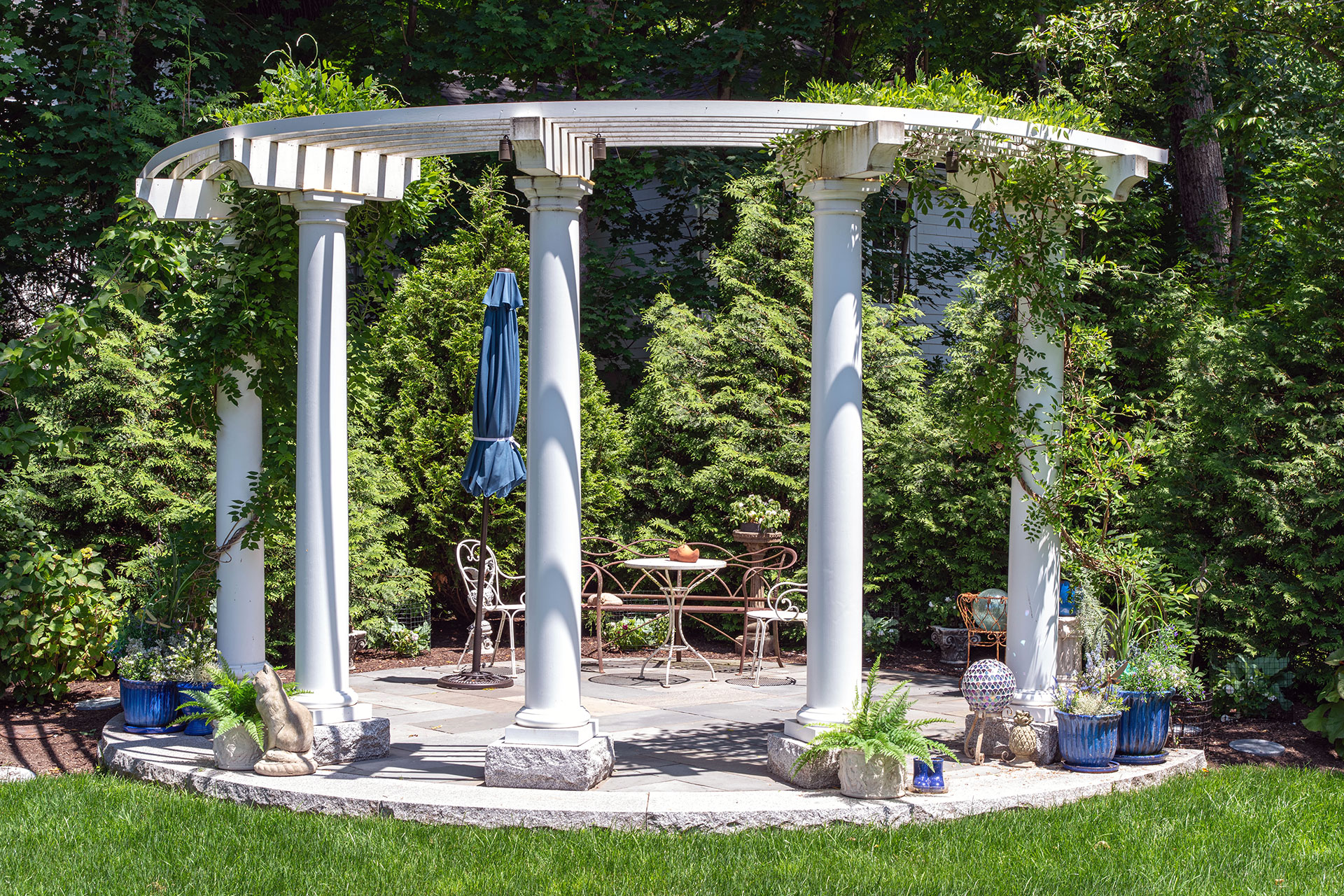 Circular pergola with classical columns creates a focal point within the garden, offering shade, symmetry, and timeless architectural appeal.