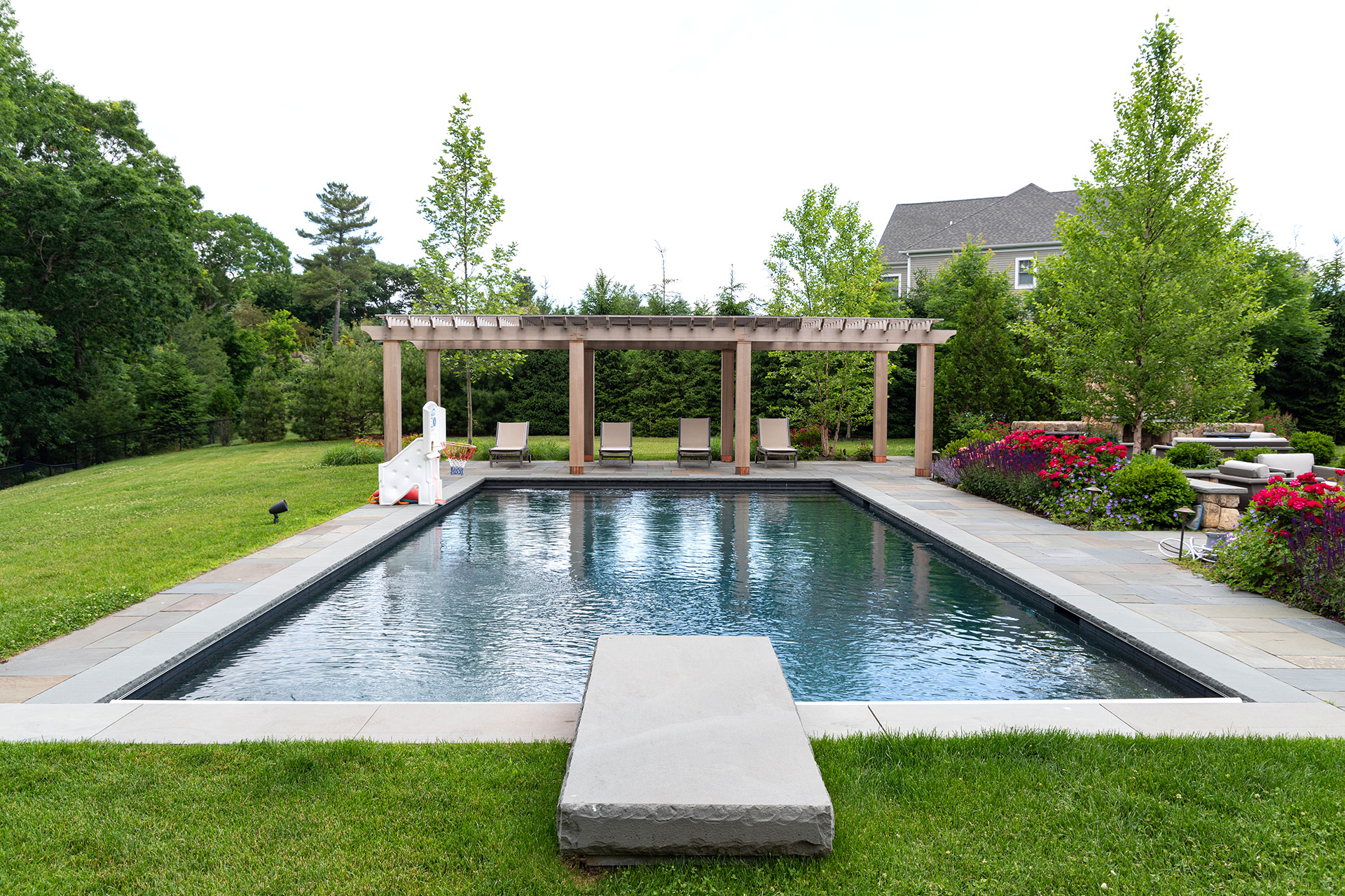 Long pergola structure enhances poolside entertaining by creating shade, guiding circulation, and visually extending the landscape design.