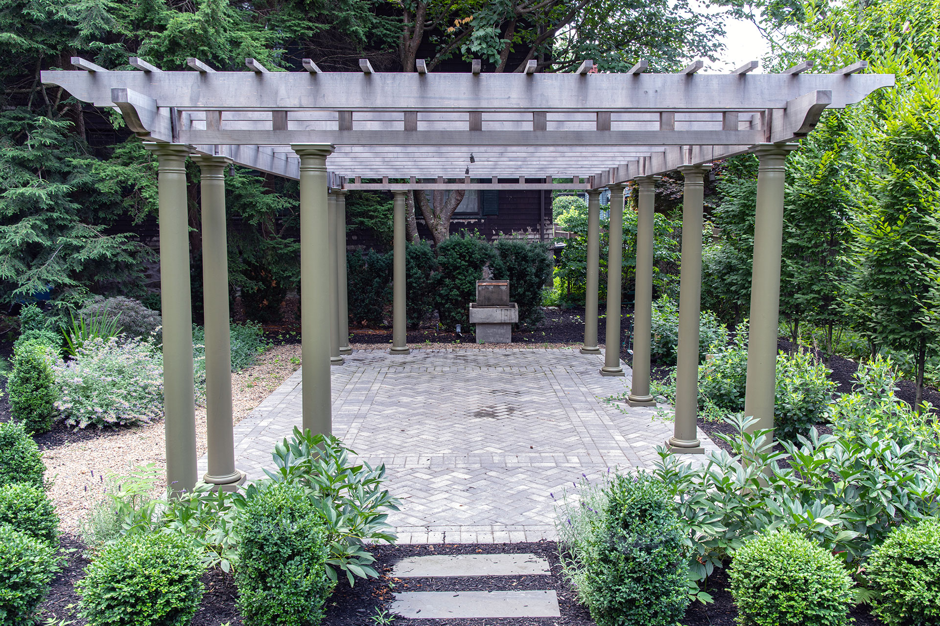 Painted wood pergola with classic columns frames a garden setting, adding elegance, vertical interest, and a sense of destination.