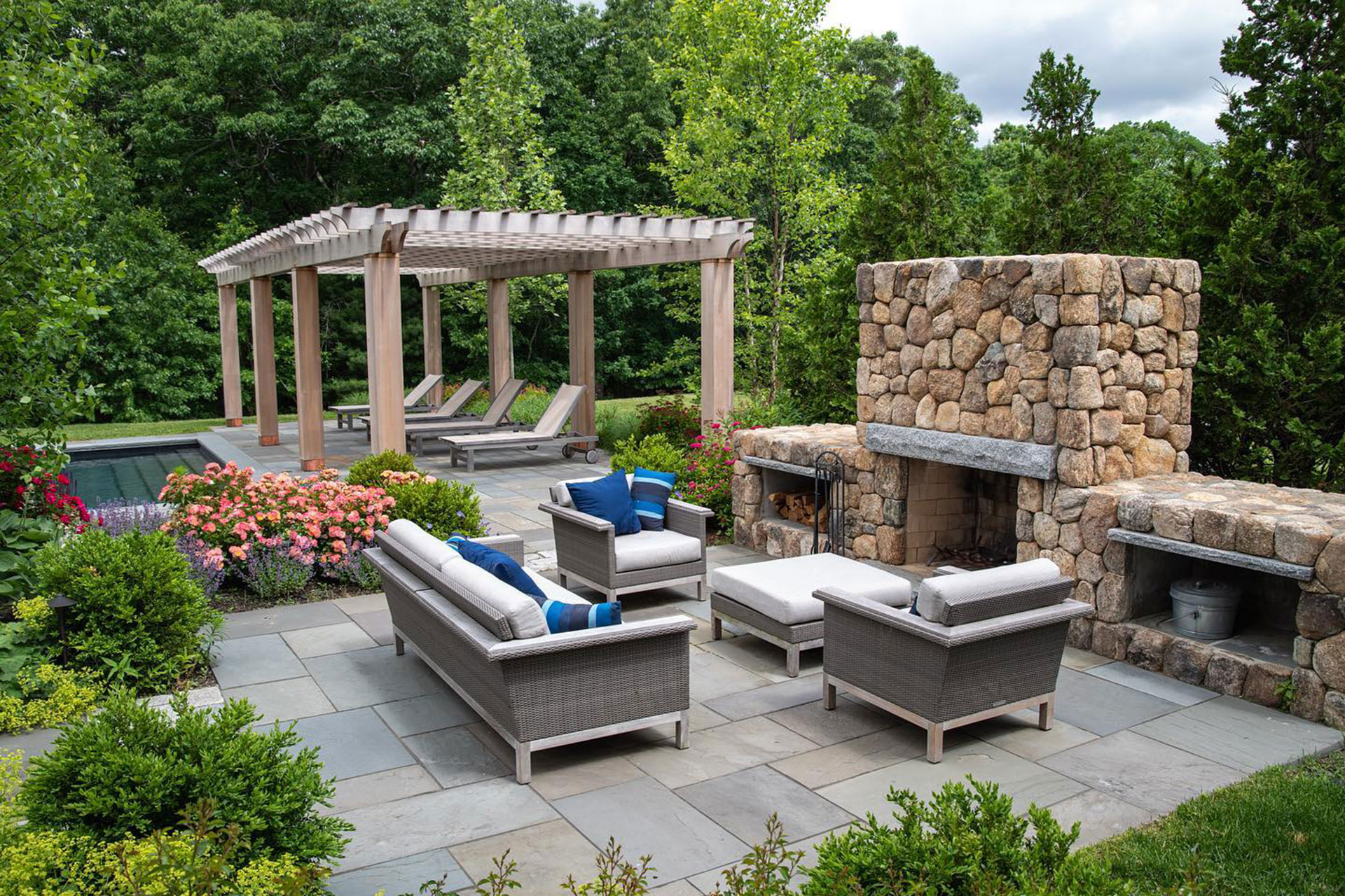 Wood pergola with stone fireplace anchors a poolside living area, enabling multi-season use and dramatic visual impact.