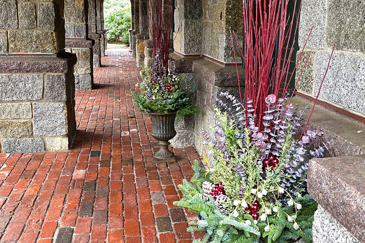 A historic arcade urn dressed with evergreen boughs and red twig accents creates a dramatic holiday display that holds up through winter.