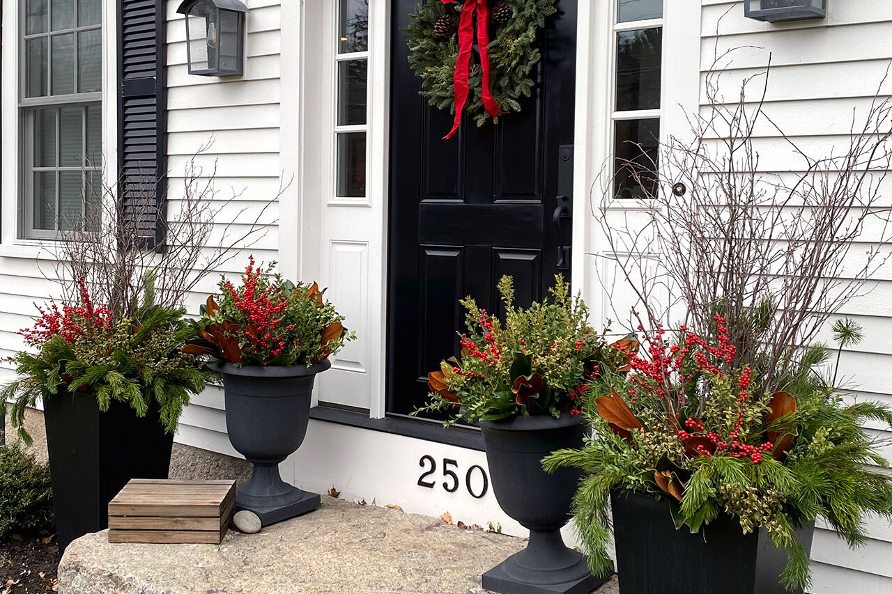 Black entry urns filled with winter evergreens frame the front door, offering strong contrast and a repeatable seasonal design.