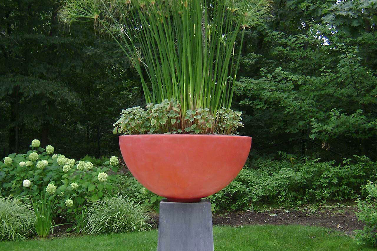 A pedestal bowl planted with ornamental grass acts as a sculptural garden feature, adding height and movement with minimal seasonal upkeep.