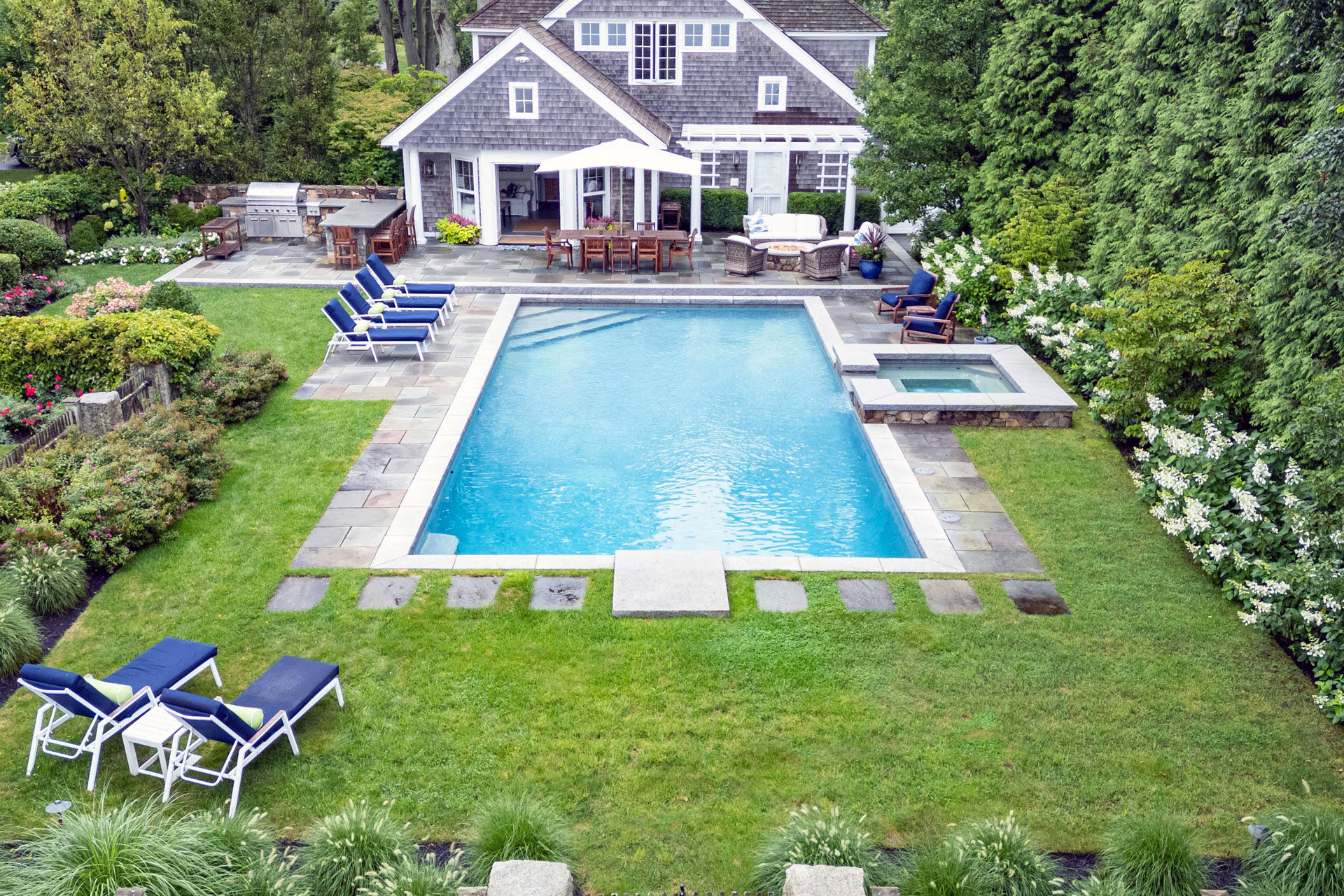 An aerial view highlighting a rectangular pool with an integrated spa and stone patio, showing how geometry and layout organize a coastal estate landscape.