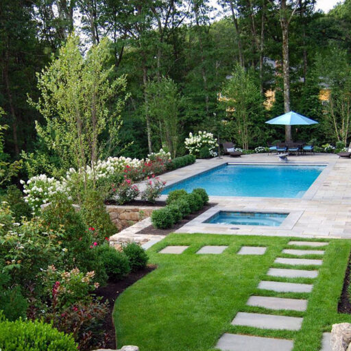 A bluestone-lined rectangular pool with an integrated spa nestled into a woodland garden, offering a quiet retreat that feels connected to its natural surroundings.