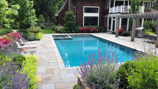 Surrounded by flowering borders and a bluestone patio, this rectangular pool blends formal structure with seasonal color, creating a garden-focused swimming environment.