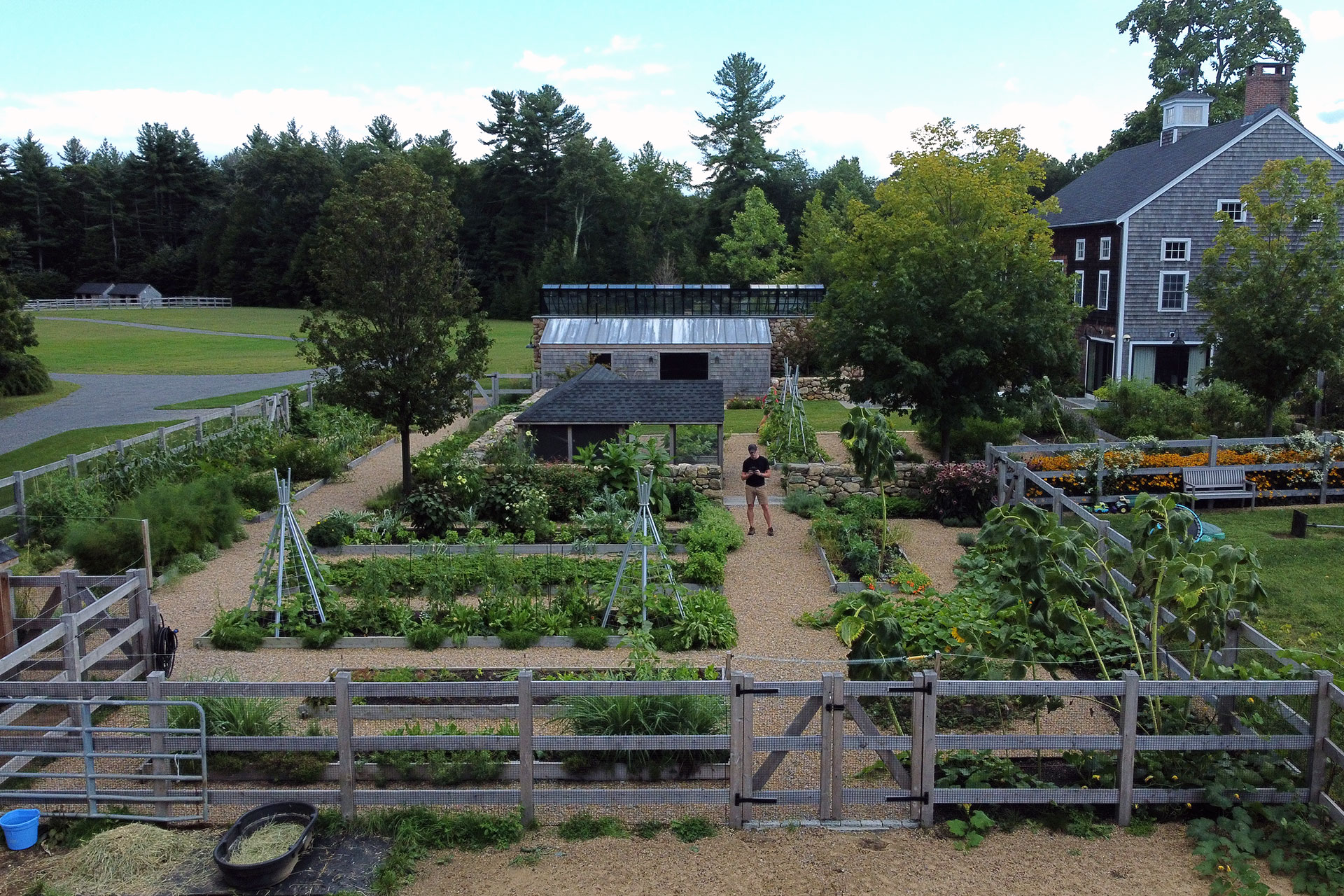 A fenced farmstead vegetable garden uses raised beds to manage soil, drainage, and wildlife pressure common in rural areas.