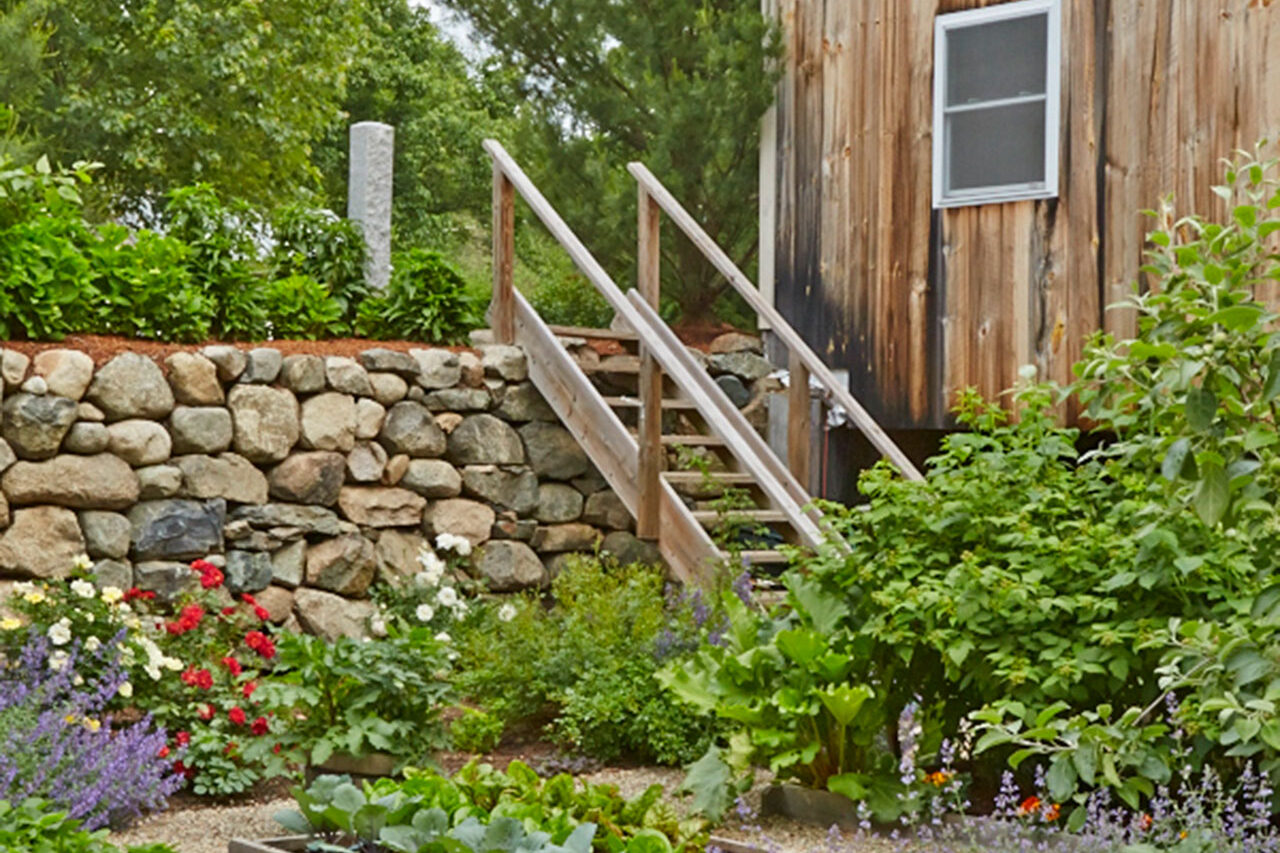 Wood steps connect raised herb beds to a shed, creating easy access and organization for seasonal gardening in New England.