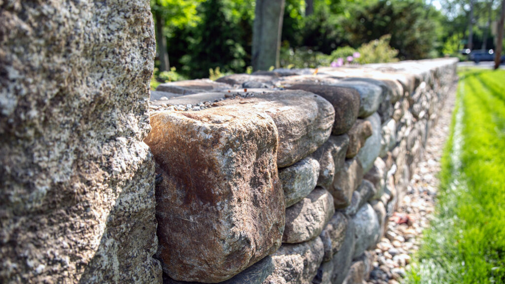 A fieldstone retaining wall manages the hillside grade, with granite steps providing a durable and clearly defined path through the slope.