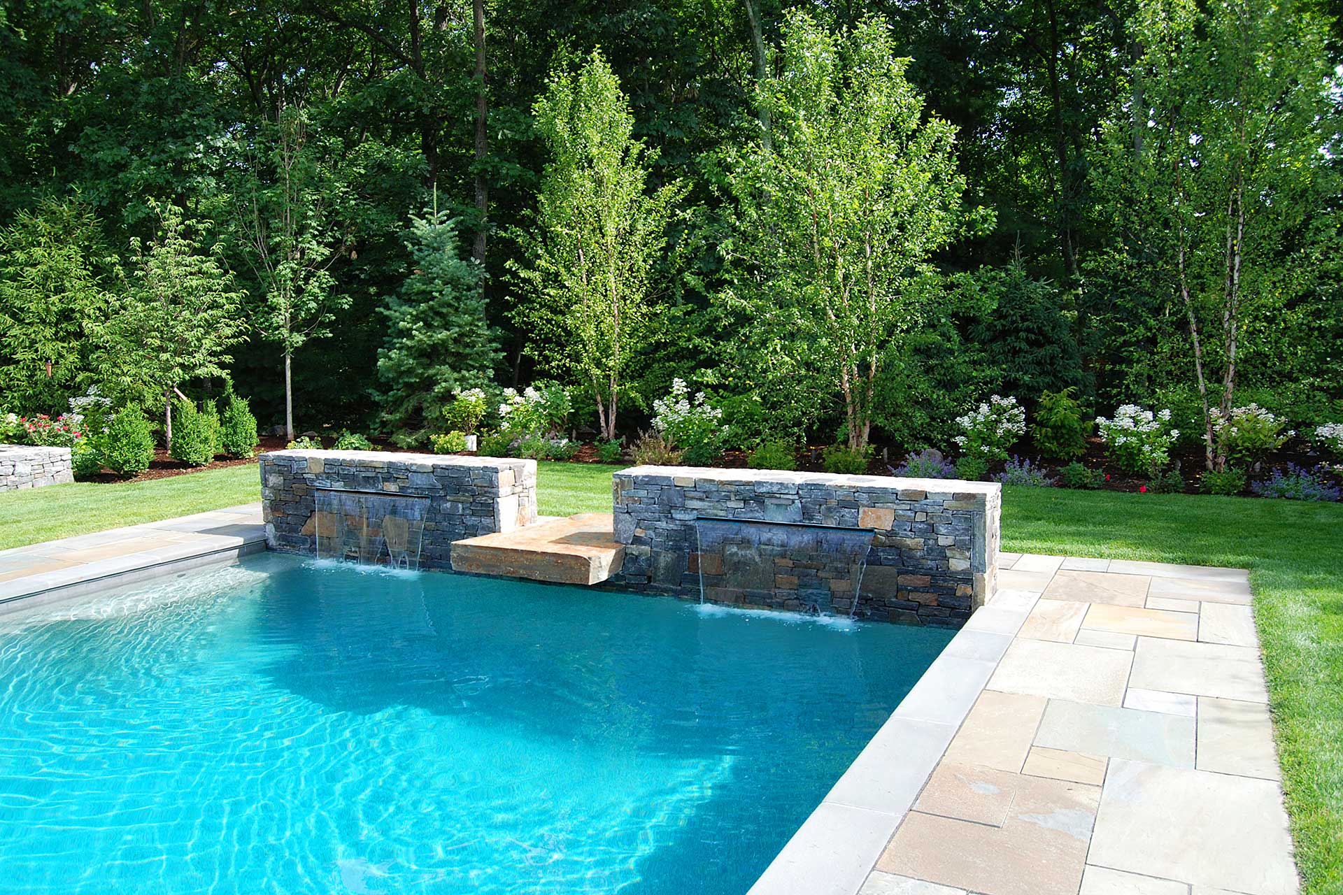 Twin stone water walls bring clean lines, sound, and movement to this modern Dover pool, adding a refined focal point without visual clutter.