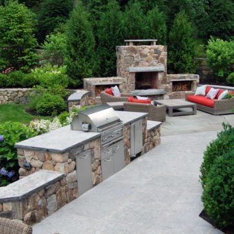 Wellesley, MA - Lush evergreen and flowering shrub plantings soften this cozy fieldstone fireplace and built in grill.