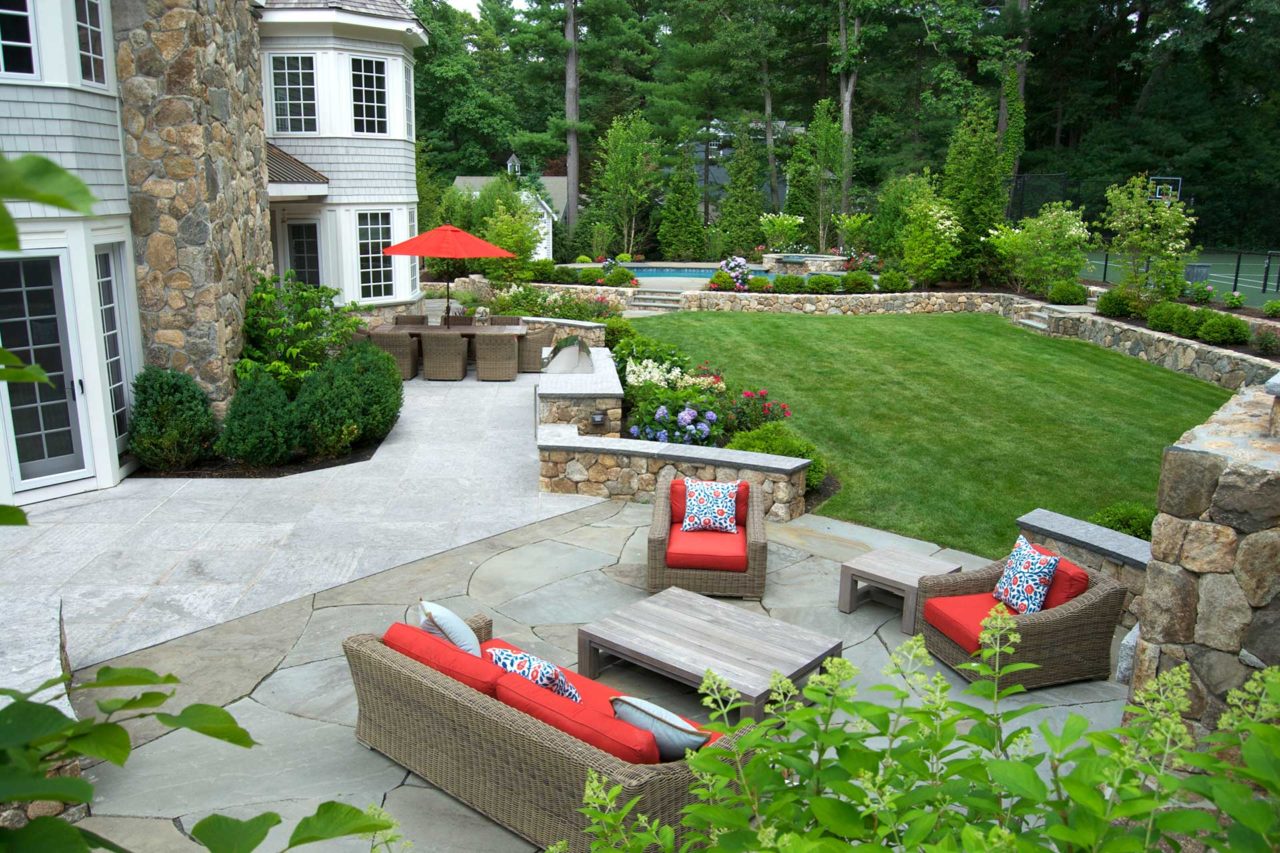 Wellesley, MA - A clear definition of outdoor living spaces: cooking and dining, gathering and relaxing, and room for play. The consistent use of stone and lush plantings join them together.