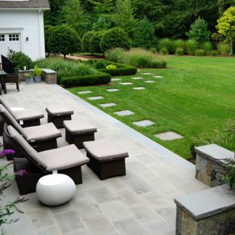 Weston, MA - Outdoor space designed for dining and gathering opens to an emerald green lawn bordered by lush planting beds.